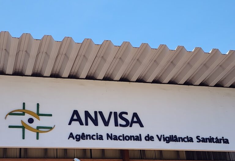Fachada da sede da Anvisa em Brasília com a placa da agência e o logotipo sobre fundo branco