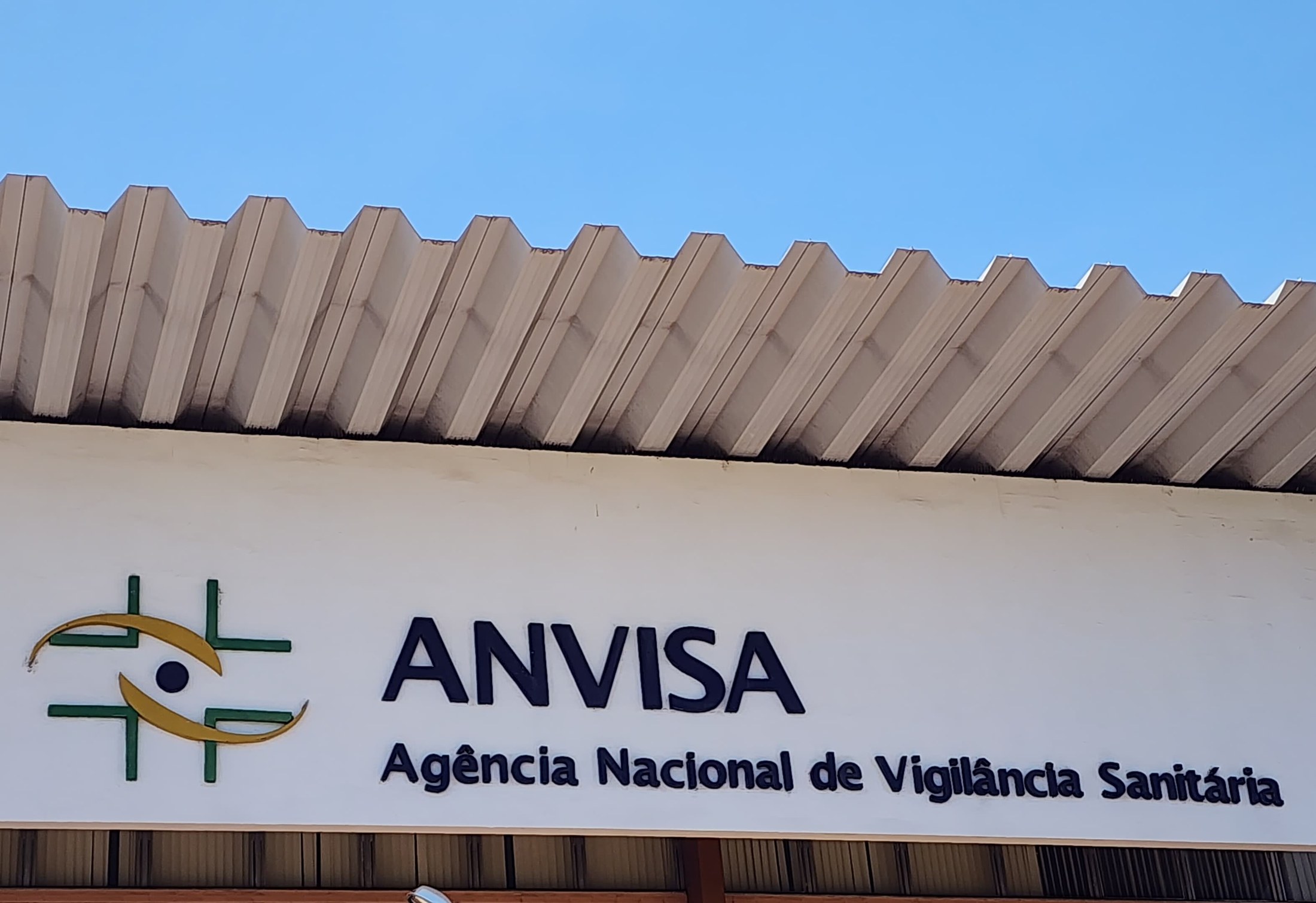 Fachada da sede da Anvisa em Brasília com a placa da agência e o logotipo sobre fundo branco