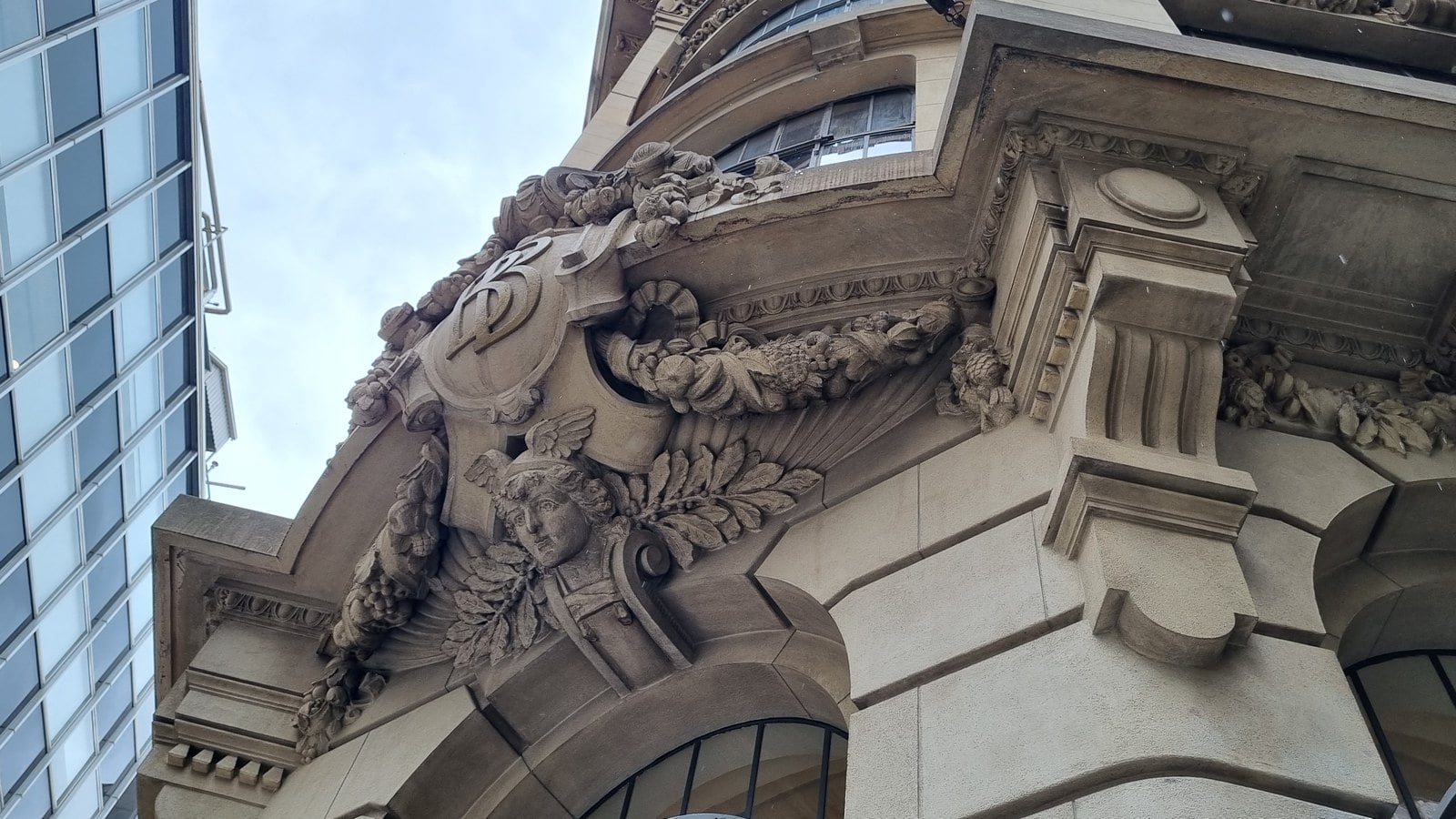 Detalhe da fachada do Centro Cultural Banco do Brasil em São Paulo, com ornamento de pedra e um edifício de vidro ao fundo