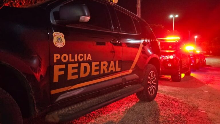 Viatura preta da Polícia Federal com giroflex ligado em rua à noite, iluminada por luz vermelha
