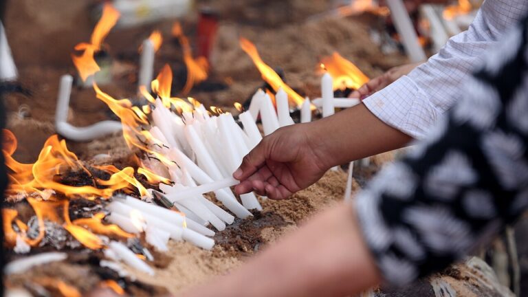 Mão acende velas em cova coberta de cera em cemitério no Dia de Finados