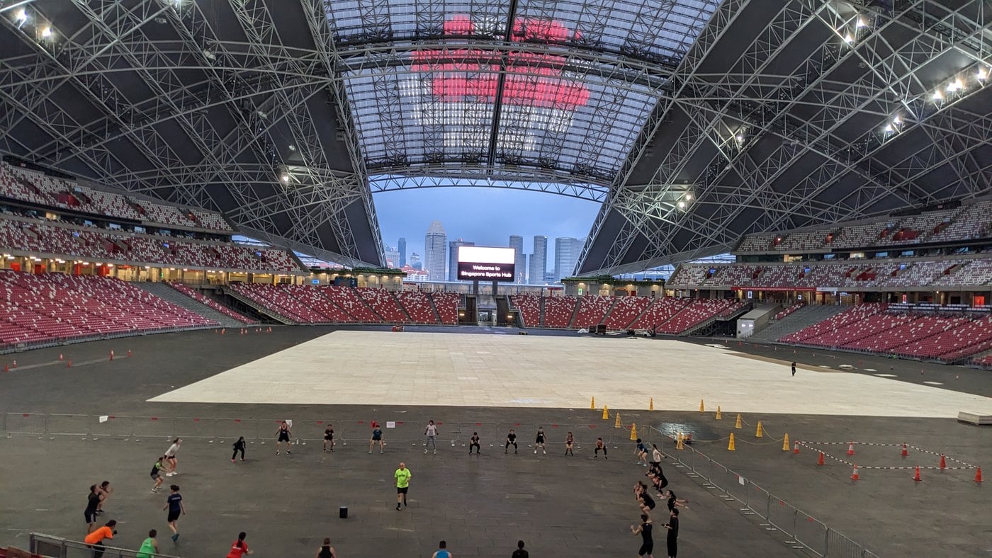 Vista interna do Estádio Nacional de Singapura, com arquibancadas vermelhas e a cobertura retrátil aberta ao fundo