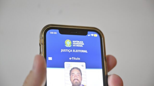 Mão segura um celular com a tela do aplicativo e-Título, que mostra a foto e os dados do eleitor