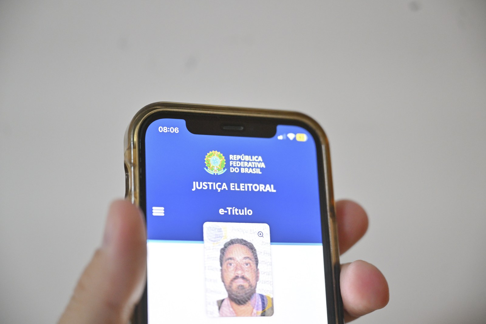 Mão segura um celular com a tela do aplicativo e-Título, que mostra a foto e os dados do eleitor