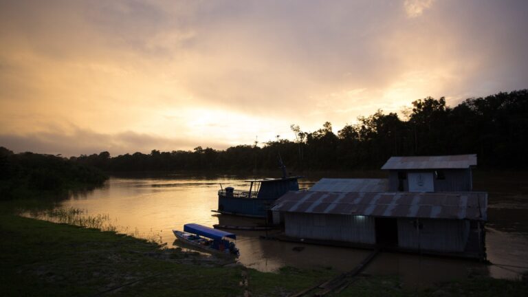 Balsa e barcos atracados em base flutuante da Funai à beira de um rio no Vale do Javari (AM), ao anoitecer