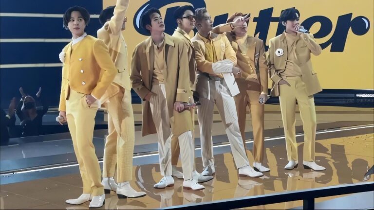 Sete integrantes do BTS no palco, vestindo ternos amarelos, durante apresentação no American Music Awards de 2021