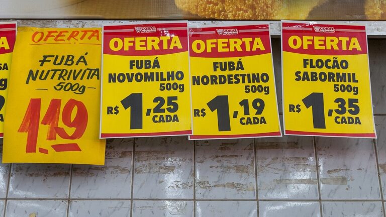 Cartazes amarelos de oferta com preços de fubá e flocão de milho em mercado brasileiro