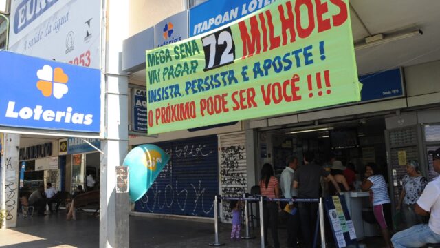 Fila de apostadores em frente a uma casa lotérica com faixa da Mega-Sena na fachada