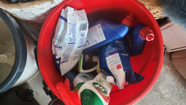 Balde vermelho com frascos e sachês de produtos de limpeza de uso doméstico