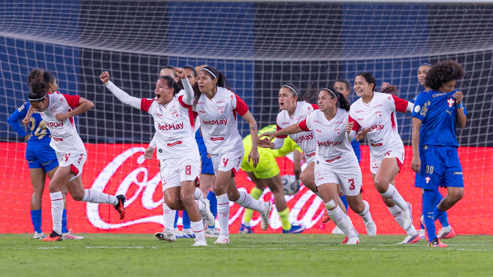 Jogadoras do Santa Fe comemoram de braços erguidos após a classificação nos pênaltis, com jogadoras do Palmeiras de cabeça baixa ao fundo